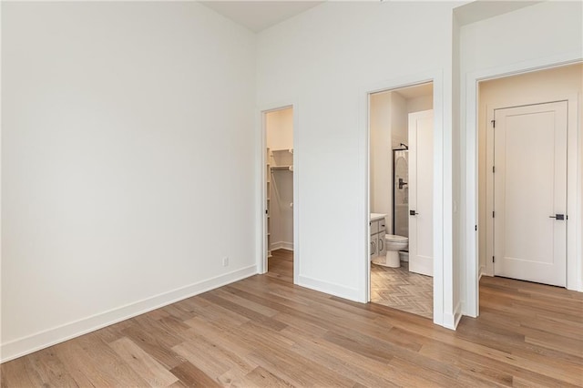 unfurnished bedroom with a closet, a spacious closet, ensuite bath, and light hardwood / wood-style flooring