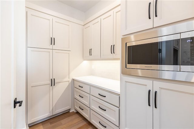 kitchen with tasteful backsplash, white cabinetry, stainless steel microwave, and light hardwood / wood-style flooring