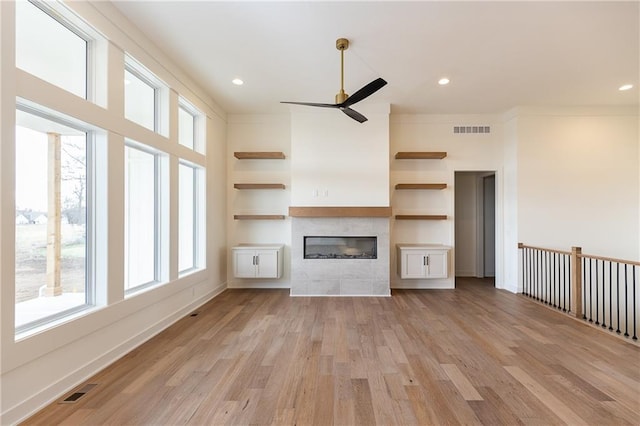 unfurnished living room with a tiled fireplace, ceiling fan, and light wood-type flooring