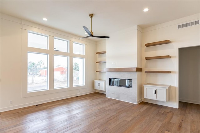 unfurnished living room with a tile fireplace, light hardwood / wood-style floors, and ceiling fan