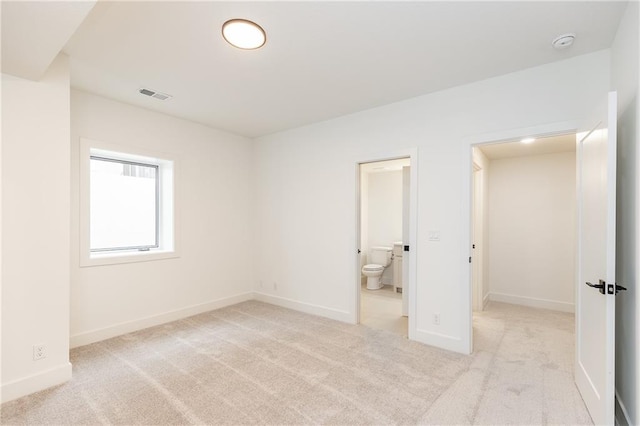 unfurnished bedroom featuring light colored carpet and ensuite bathroom