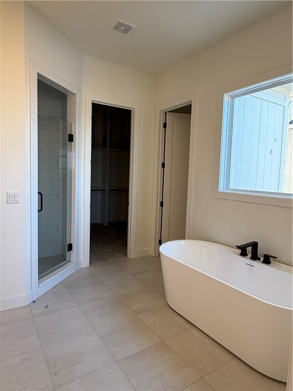 bathroom featuring a stall shower, a freestanding tub, visible vents, and baseboards