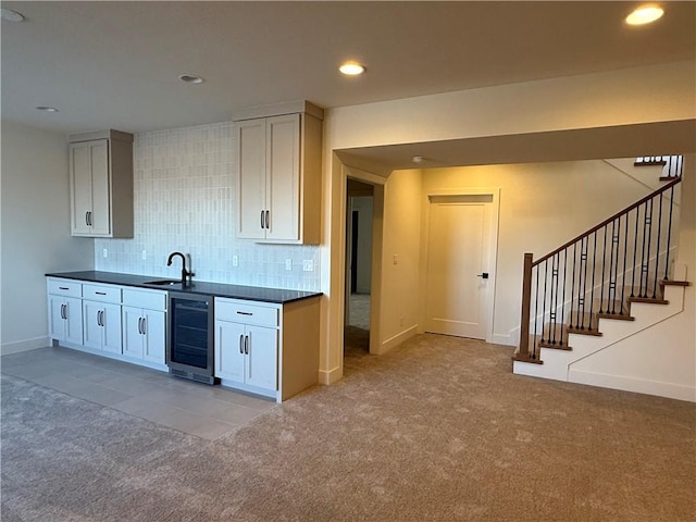 kitchen with dark countertops, wine cooler, a sink, and light colored carpet