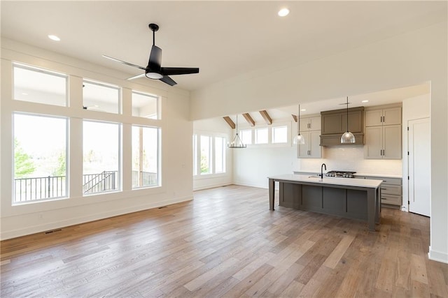kitchen with ceiling fan, light wood-style floors, light countertops, decorative backsplash, and a center island with sink