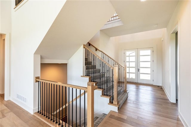 stairs with french doors, wood finished floors, visible vents, and baseboards