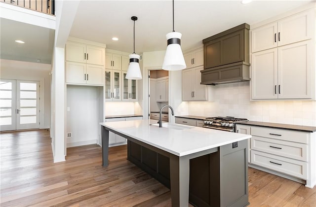 kitchen featuring light countertops, hanging light fixtures, glass insert cabinets, a kitchen island with sink, and a sink