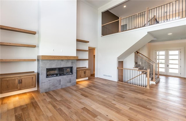 unfurnished living room featuring french doors, visible vents, a tiled fireplace, light wood-style floors, and stairs