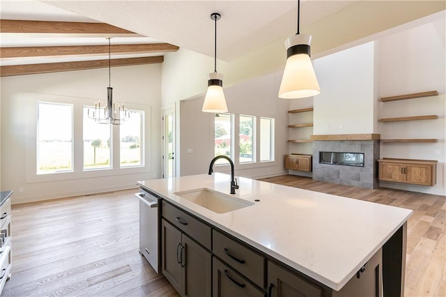 kitchen with a kitchen island with sink, a sink, open floor plan, stainless steel dishwasher, and decorative light fixtures