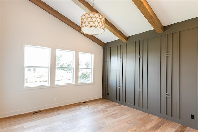 empty room featuring light wood-type flooring, plenty of natural light, lofted ceiling with beams, and baseboards