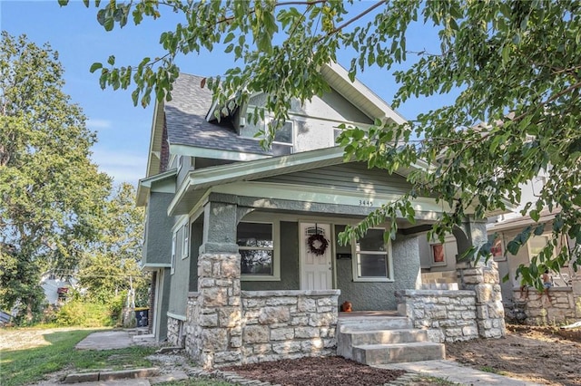 view of front of home with stucco siding, stone siding, covered porch, and a shingled roof