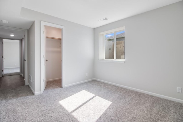 unfurnished bedroom with a walk in closet, a closet, and carpet flooring