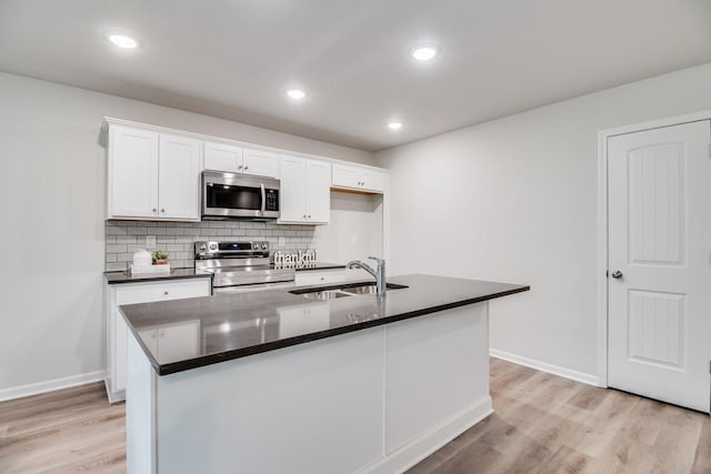 kitchen with sink, appliances with stainless steel finishes, tasteful backsplash, white cabinets, and a center island with sink