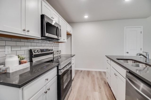 kitchen with sink, appliances with stainless steel finishes, white cabinetry, light hardwood / wood-style floors, and decorative backsplash