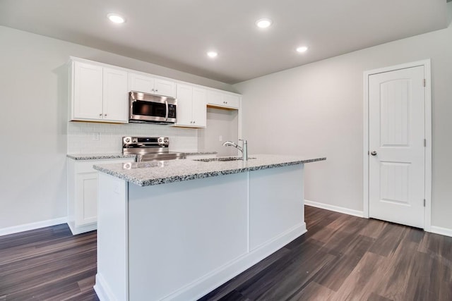 kitchen with sink, stainless steel appliances, light stone countertops, white cabinets, and a center island with sink