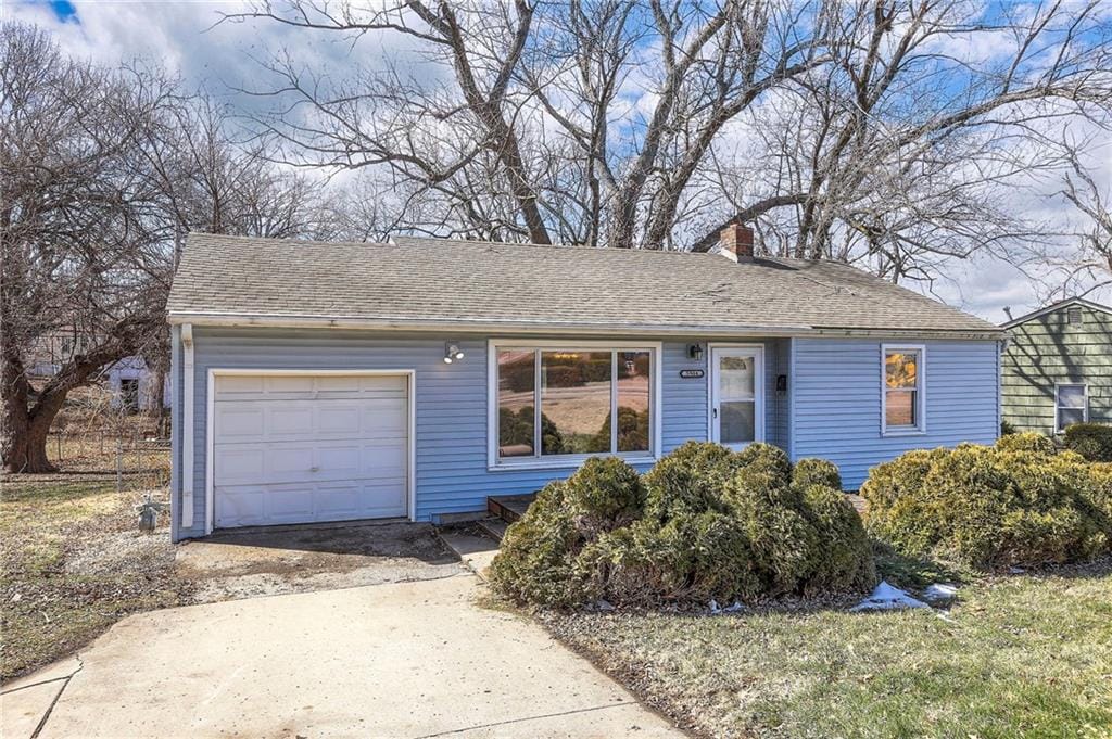 ranch-style house featuring an attached garage, a chimney, concrete driveway, and roof with shingles