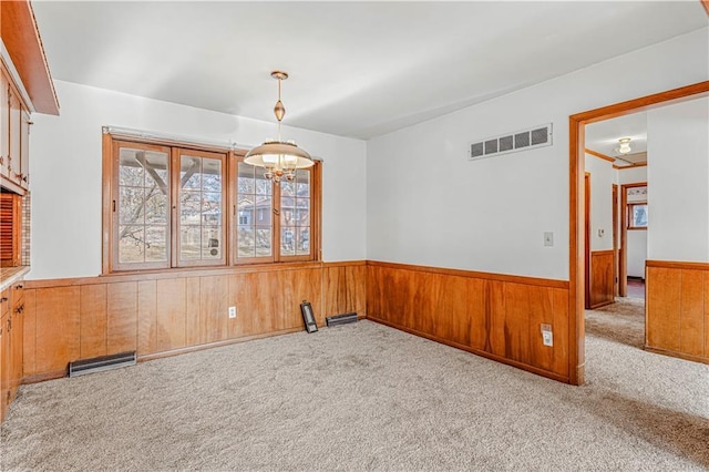 spare room featuring a chandelier, wood walls, and light carpet