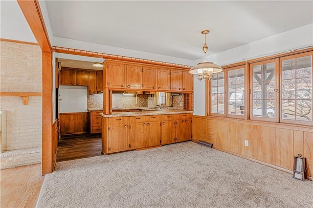 kitchen with hanging light fixtures, backsplash, kitchen peninsula, wood walls, and light carpet