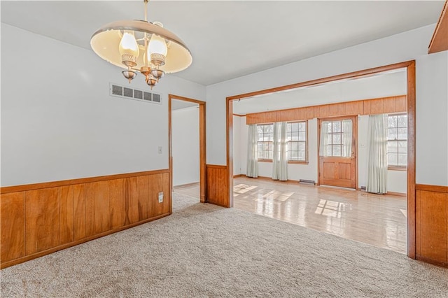 unfurnished room featuring light colored carpet, an inviting chandelier, and wood walls