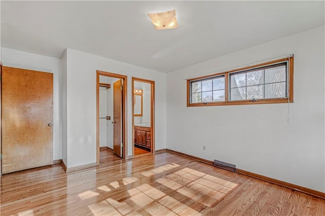 unfurnished bedroom featuring ensuite bathroom and light hardwood / wood-style flooring