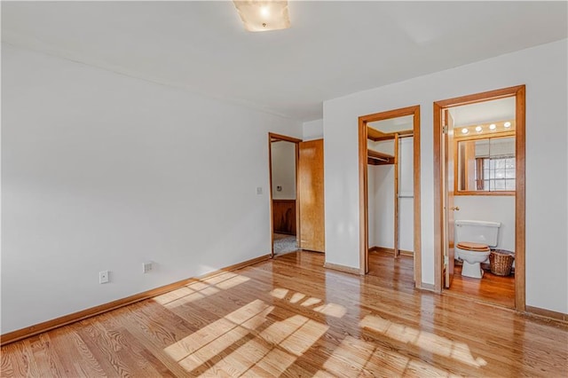 unfurnished bedroom with a walk in closet, ensuite bathroom, a closet, and light hardwood / wood-style floors