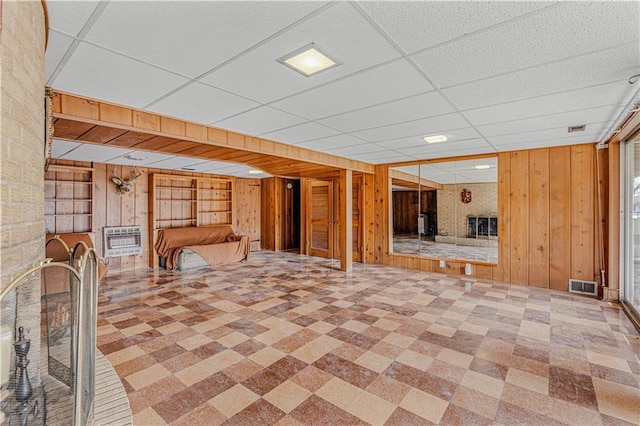 basement with heating unit, wood walls, a drop ceiling, and built in features