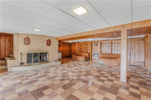 unfurnished living room with a fireplace, a drop ceiling, and wood walls