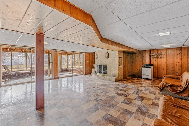 unfurnished living room featuring a paneled ceiling, wood walls, a healthy amount of sunlight, and a brick fireplace