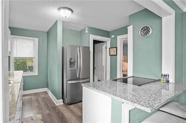 kitchen featuring kitchen peninsula, light stone counters, wood-type flooring, and stainless steel fridge with ice dispenser