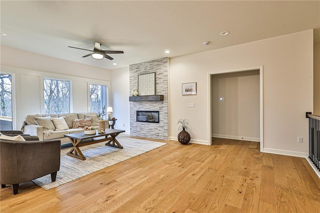 living room featuring ceiling fan, a fireplace, and light hardwood / wood-style flooring