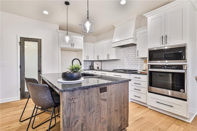 kitchen featuring appliances with stainless steel finishes, light hardwood / wood-style flooring, premium range hood, and a center island with sink