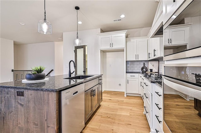 kitchen featuring white cabinets, light hardwood / wood-style floors, appliances with stainless steel finishes, and an island with sink