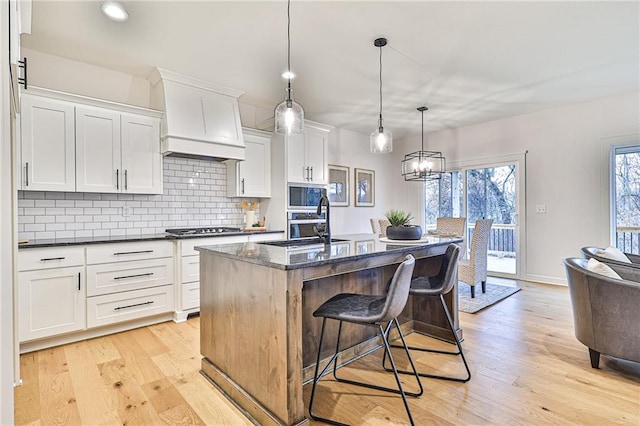 kitchen with decorative backsplash, stainless steel appliances, custom exhaust hood, and light hardwood / wood-style flooring