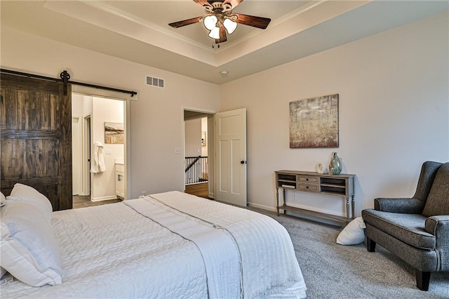 bedroom with a tray ceiling, ensuite bath, carpet, a barn door, and ceiling fan