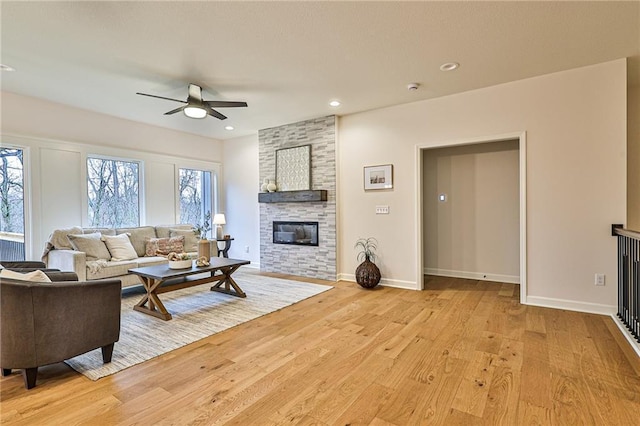 living room featuring a fireplace, light wood-type flooring, and ceiling fan