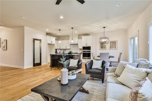 living room with ceiling fan with notable chandelier and light hardwood / wood-style floors