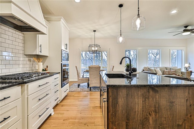 kitchen with dark stone counters, premium range hood, tasteful backsplash, appliances with stainless steel finishes, and light hardwood / wood-style flooring