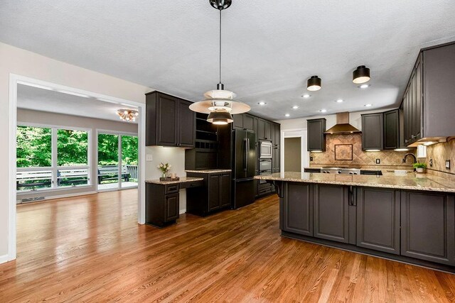 kitchen featuring black refrigerator, pendant lighting, stainless steel microwave, light hardwood / wood-style floors, and wall chimney exhaust hood