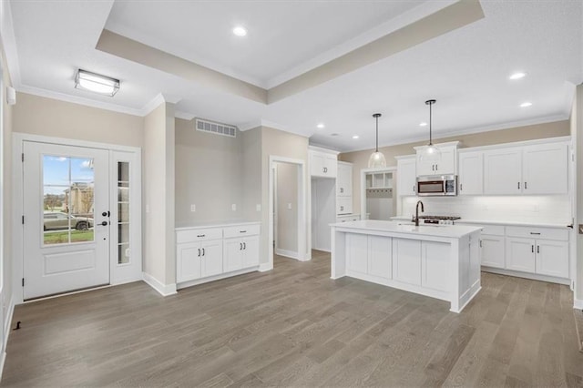 kitchen featuring white cabinetry, backsplash, pendant lighting, light hardwood / wood-style floors, and a center island with sink