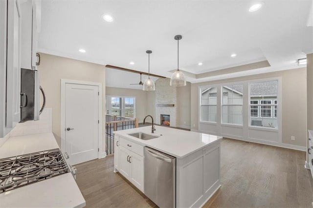 kitchen with dishwasher, a center island with sink, white cabinets, sink, and a tray ceiling