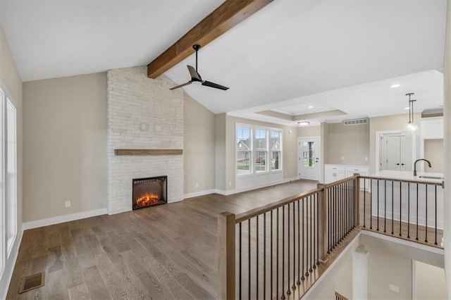 unfurnished living room featuring ceiling fan, sink, hardwood / wood-style flooring, a fireplace, and vaulted ceiling with beams