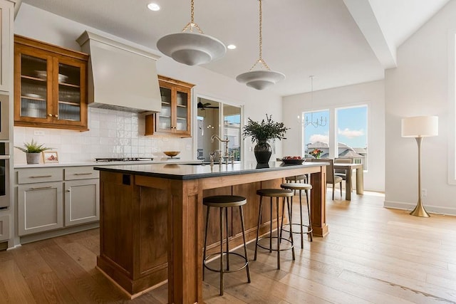 kitchen featuring pendant lighting, sink, a center island with sink, and premium range hood