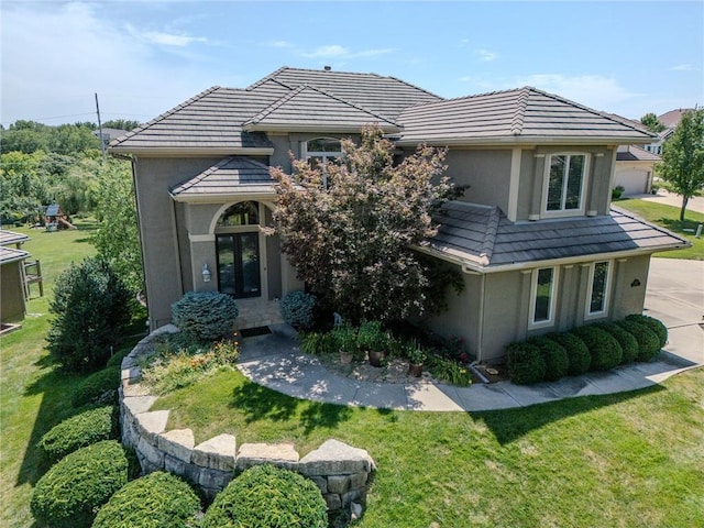 rear view of property featuring a tile roof, a lawn, french doors, and stucco siding