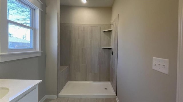 full bathroom with baseboards, tiled shower, and vanity