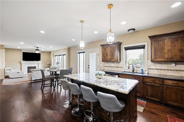 kitchen featuring dark hardwood / wood-style floors, sink, hanging light fixtures, decorative backsplash, and light stone countertops