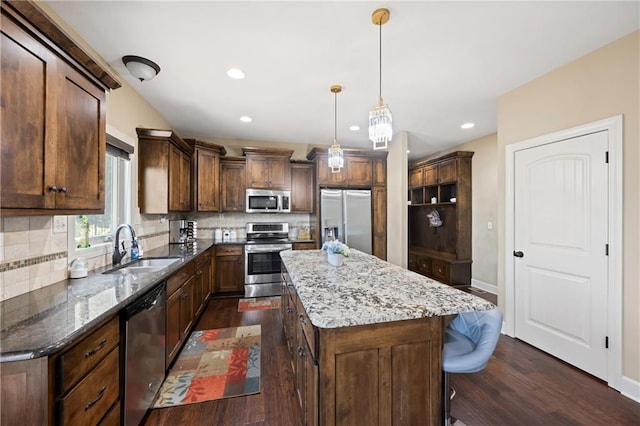 kitchen with sink, a kitchen island, stainless steel appliances, dark stone countertops, and dark hardwood / wood-style flooring