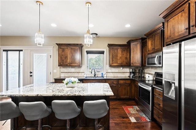 kitchen with appliances with stainless steel finishes, hanging light fixtures, dark hardwood / wood-style floors, dark stone counters, and sink