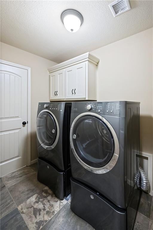 clothes washing area with a textured ceiling, separate washer and dryer, and cabinets