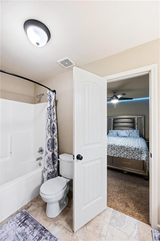 bathroom with shower / bathtub combination with curtain, ceiling fan, tile patterned floors, and toilet