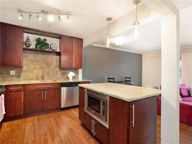 kitchen with stainless steel appliances, pendant lighting, sink, a kitchen island, and light hardwood / wood-style floors