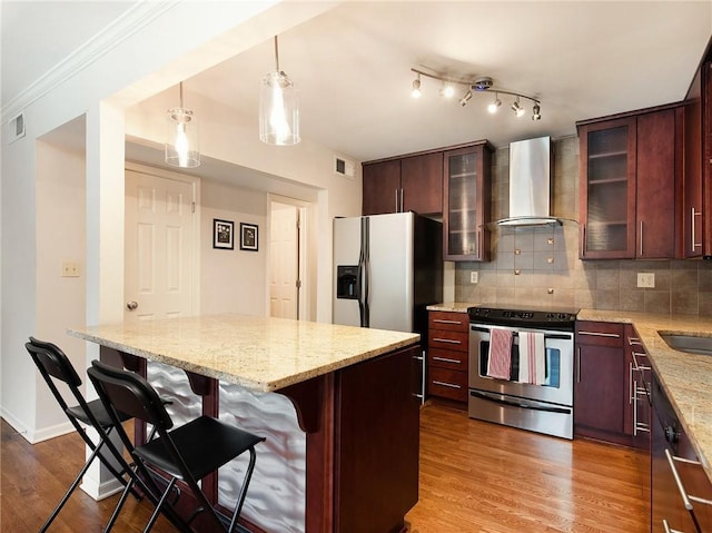 kitchen featuring appliances with stainless steel finishes, wall chimney range hood, hanging light fixtures, backsplash, and hardwood / wood-style flooring